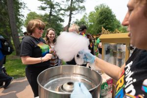 Two members of Perkins staff stand outdoors at the Perkins Pride Parade on June 6th. They are standing at the cotton candy and popcorn table, where cotton candy is being made in the foreground by another staff member